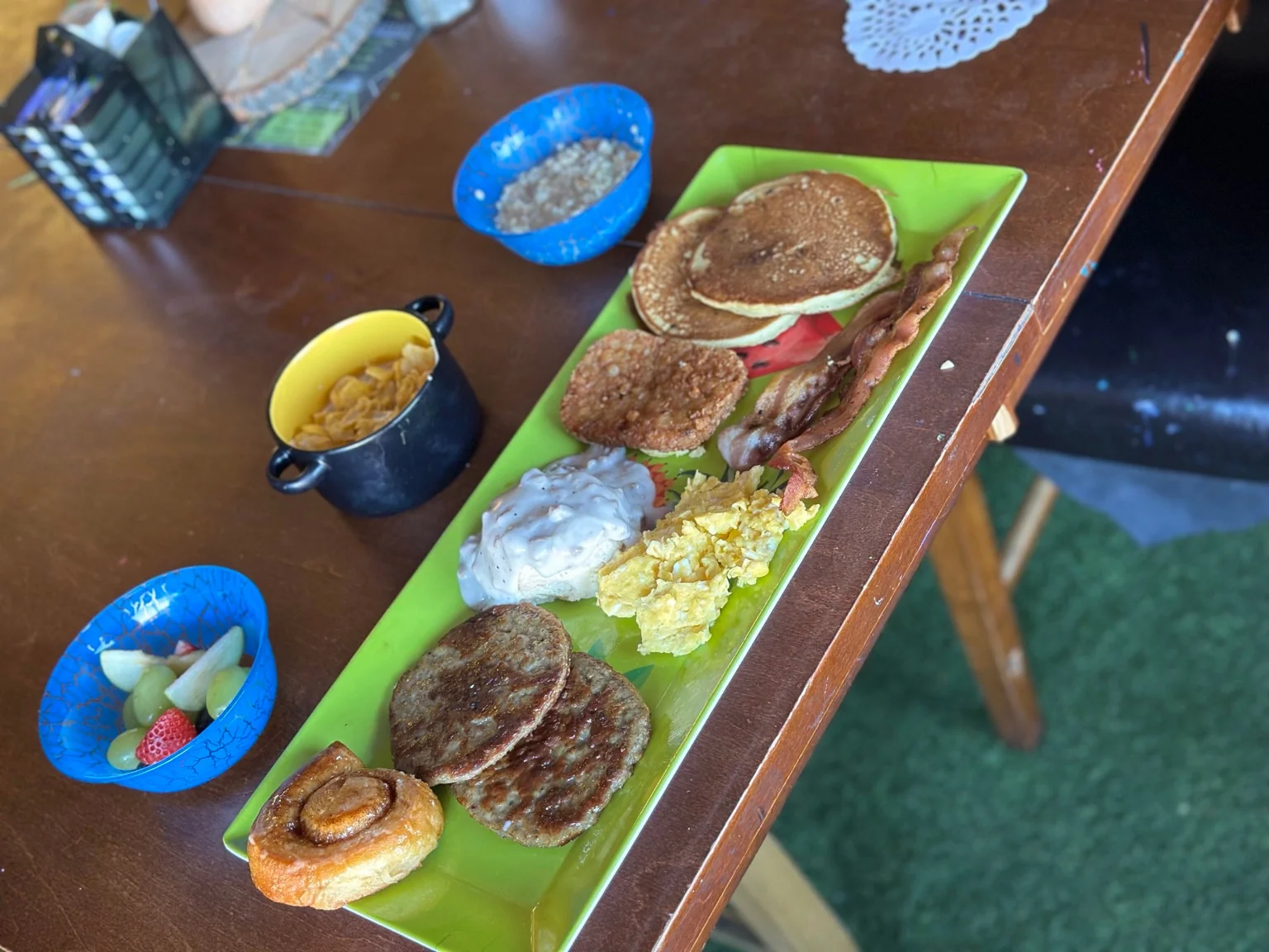 A cafe breakfast spread with pancakes, eggs, bacon, sausage and fruit