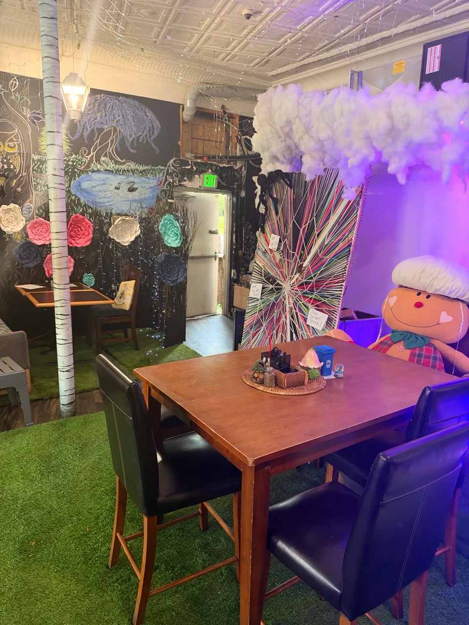 A cozy café table beneath handmade clouds, beside flower art and an owl mural