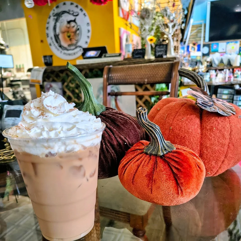 Iced Maple Cinnamon Latte with whipped cream beside fabric pumpkins in the cafe