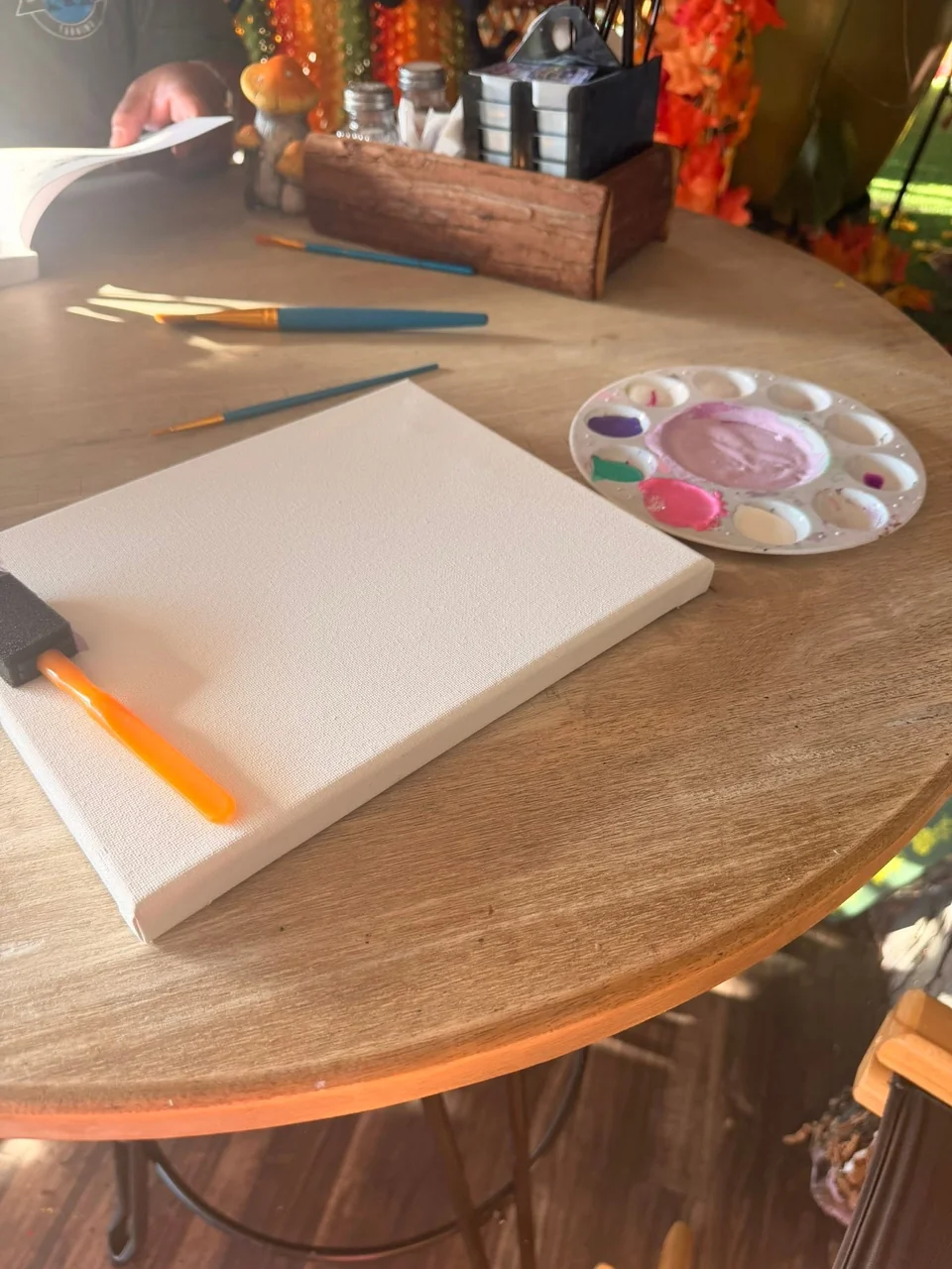 A blank canvas, paint palette and brushes ready for painting at a cafe table